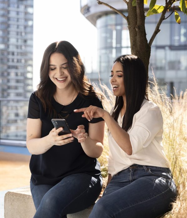 two-female-friends-rooftop-terrace-using-smartphone